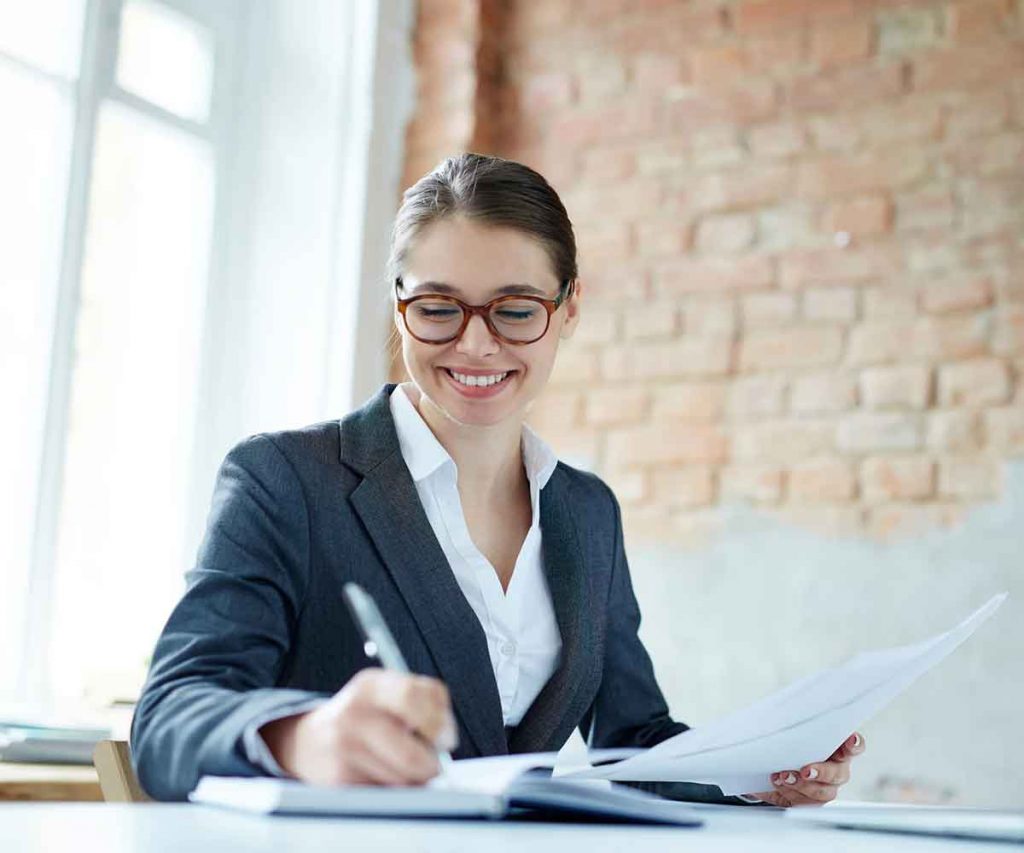 Caucasian woman in glasses smiles and writes in a notebook