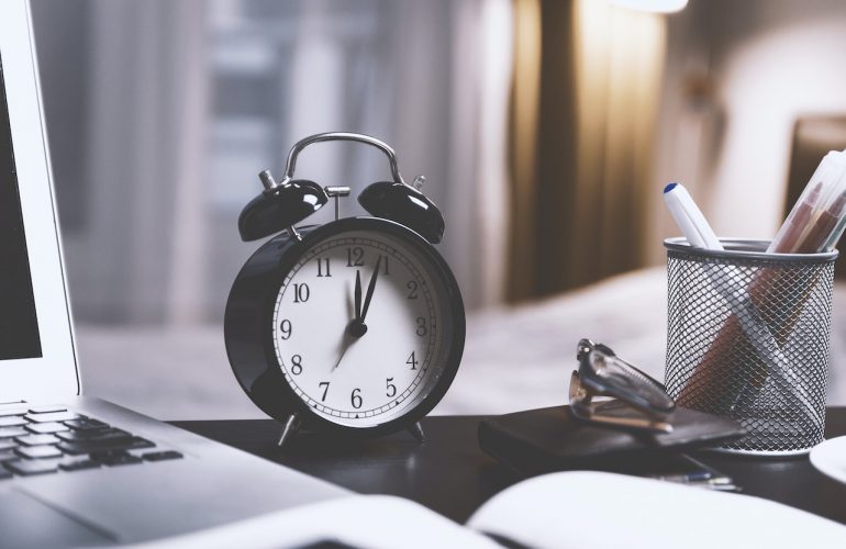 clock next to computer and pens on desk