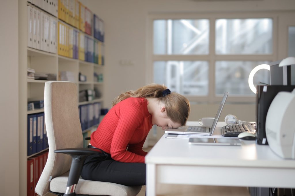 Woman sitting with head on her desk and laptop open.