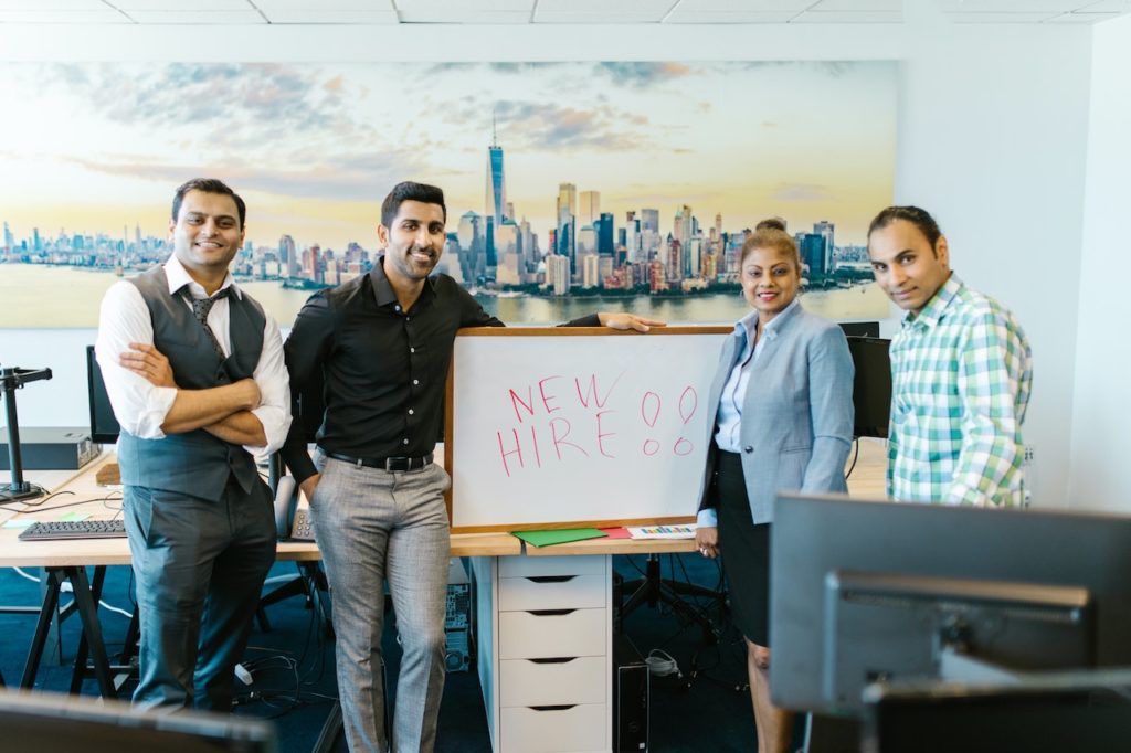 Employees in an office, holding a sign that says, "New Hire."
